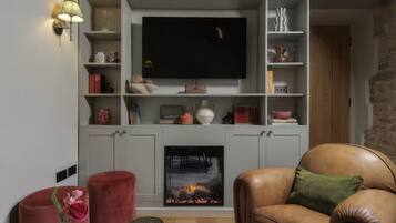 Una sala de estar con chimenea, televisor montado encima y un sillón de cuero con cojín verde.