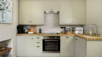 A modern kitchen with light-colored cabinets, a built-in oven, a coffee machine, and a bread container.