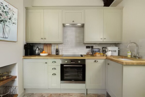 Una cucina moderna con mobili chiari, forno integrato, macchina per il caffè e contenitore per il pane.