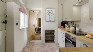 A modern kitchen with white cabinets, a wooden countertop, and a dining area with a table and chairs. - Cosy Cotswold Cottage in Bibury w/ Private Parking - Perfect Romantic Getaway (Bibury)