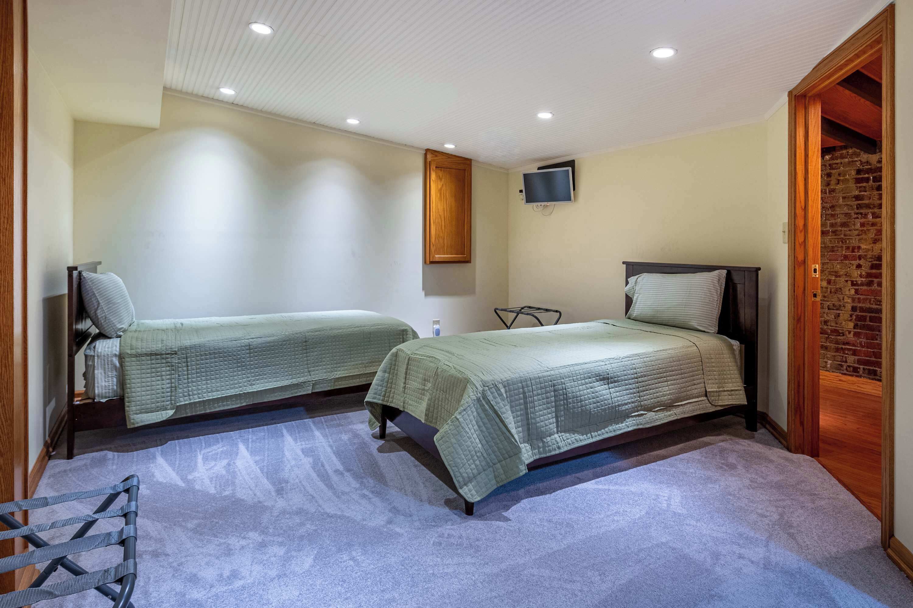 A bedroom with two beds, a TV mounted on the wall, and a brick wall on one side.