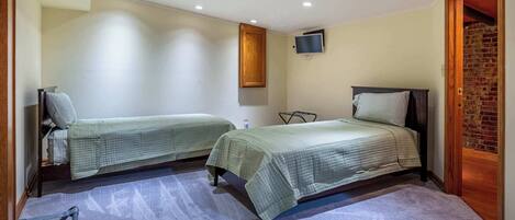 A bedroom with two beds, a TV mounted on the wall, and a brick wall on one side.