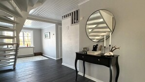 Un couloir doté d’un plancher en bois foncé, d’une console noire avec un miroir et d’une porte blanche.