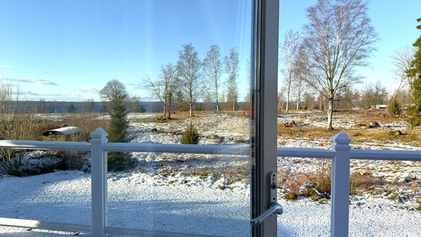 Une vue à travers une fenêtre ornée d’une balustrade blanche, donnant sur un paysage enneigé avec des arbres et un ciel dégagé.