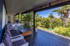 Un espacio de estar al aire libre techado, con piso de madera, asientos blancos y morados y vistas a un jardín exuberante.