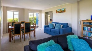 A spacious living room with a blue sofa, a dining area with wooden chairs, and a bookshelf.