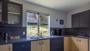 A modern kitchen with dark cabinets, a large window, and a view of a garden.