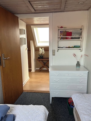 Ein Schlafzimmer mit Dachfenster, einem weißen Schminktisch, einem Regal mit Spielzeug und einem Bett mit blauem Kopfkissen.