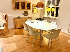 A dining area with a round table, chairs, a wooden cabinet, and a window with blinds. - Cosy townhouse in the heart of beautiful Bagenkop (Bagenkop)