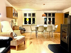 A living room with a dining area, a kitchen with a stove, and a window with blinds.