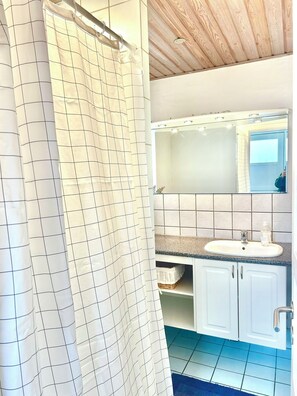 Ein Badezimmer mit Duschvorhang, Waschbecken, Spiegel und Fliesenwänden.
