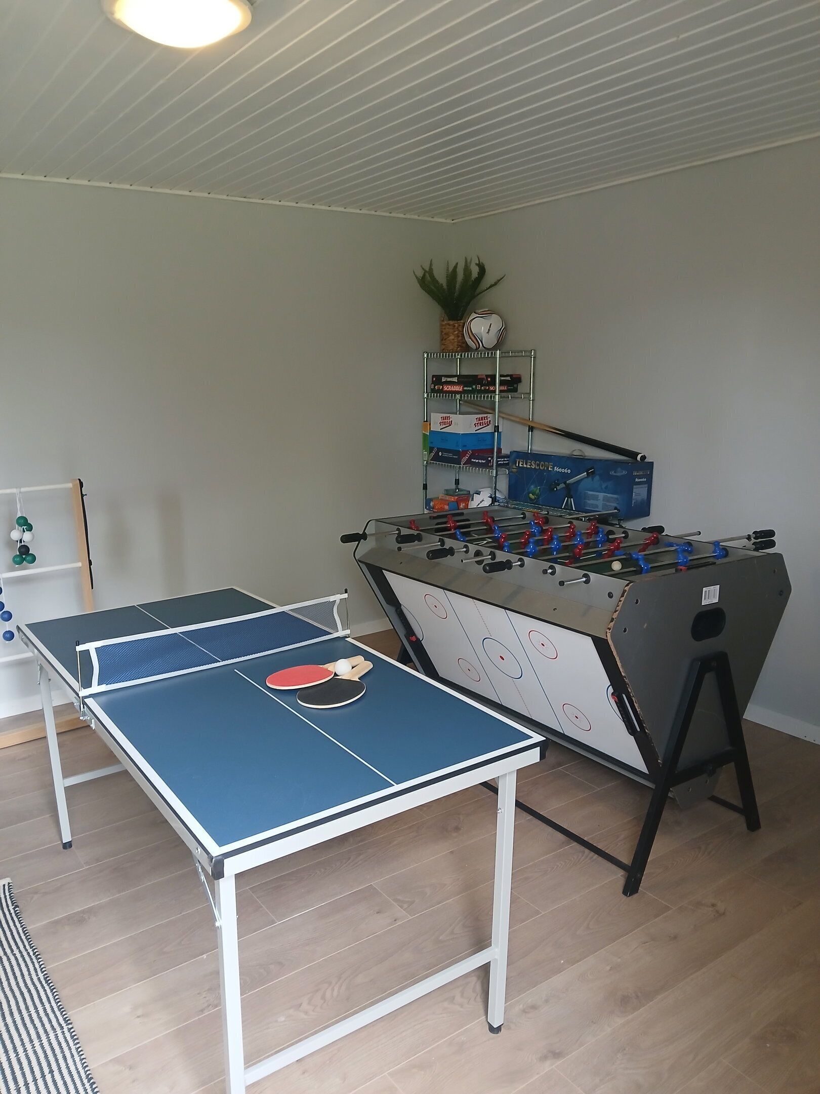 Une table de ping-pong, une table de baby-foot et une étagère remplie de jeux de société.