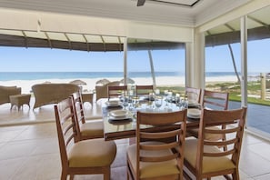 Zona pranzo con vista sulla spiaggia, arredi in vimini e tavolo in vetro imbandito per quattro persone.