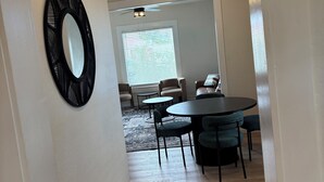 Un salon moderne avec une table ronde et des chaises, un ventilateur de plafond et une grande fenêtre avec des stores.