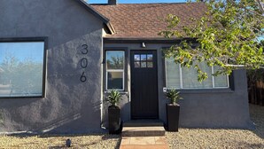 Une maison de plain-pied avec une porte marron foncé, deux fenêtres et un petit porche.