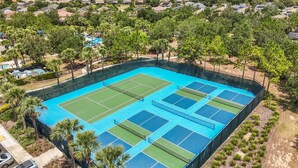 Ein großer Tennisplatz im Freien, umgeben von Bäumen und Wohnhäusern.