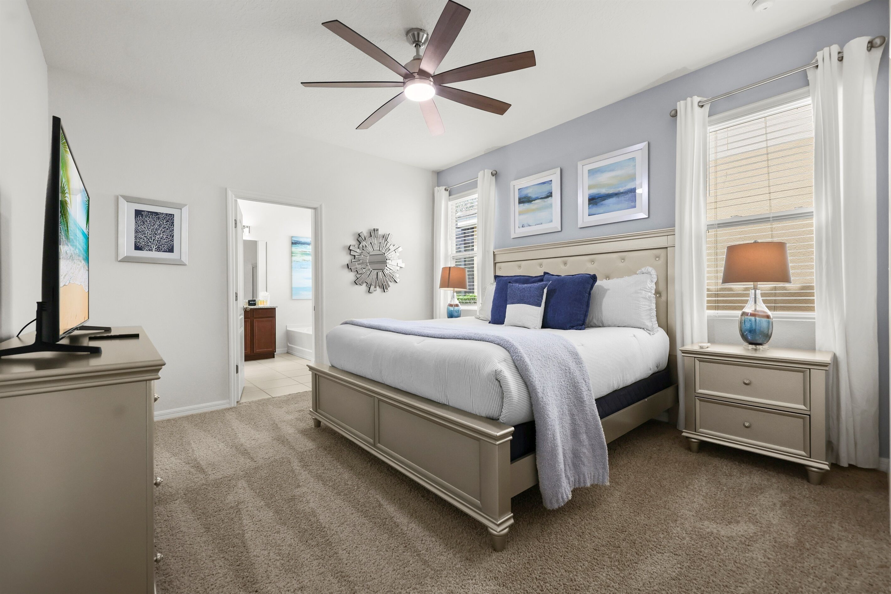 A bedroom with a bed, nightstands, a ceiling fan, and artwork on the walls.