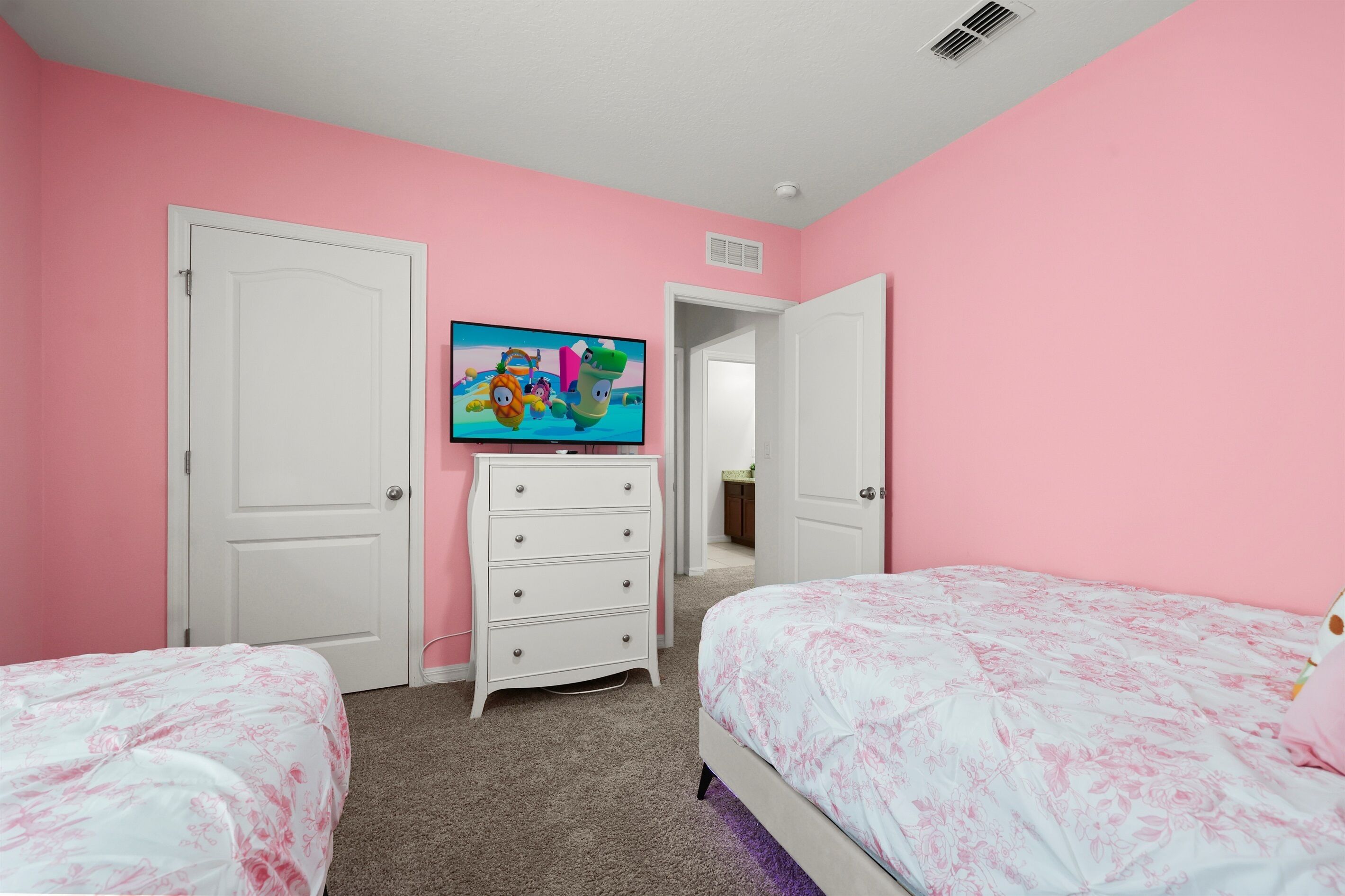 A bedroom with pink walls, a white dresser, a television, and two beds with floral bedding.