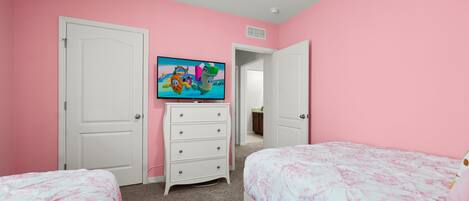 A bedroom with pink walls, a white dresser, a television, and two beds with floral bedding.
