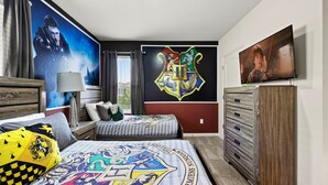 Ein Schlafzimmer mit einem Bett, einer Kommode, einem Fernseher und einer Wand mit dem Harry Potter Wappen.