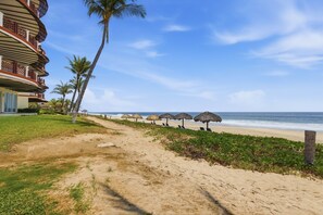 A beach with a hotel, palm trees, and thatched umbrellas.
