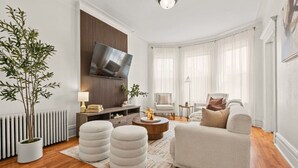 Ein modernes Wohnzimmer mit einer Couch, Hocker, einem Couchtisch und einem Fernseher, der an einer Holzwand befestigt ist.