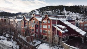 En byggnad med flera våningar, en röd fasad och ett sluttande tak, omgiven av snötäckt terräng och en skogbeklädd kulle i bakgrunden.