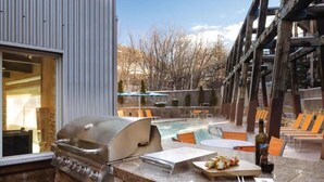 En uteplats med grill, pool, solstolar och utsikt över träd och berg.