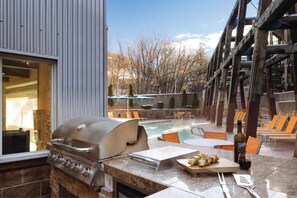 Eine Terrassenausstattung im Freien mit Grill, Pool, Liegestühlen und Blick auf Bäume und Berge.