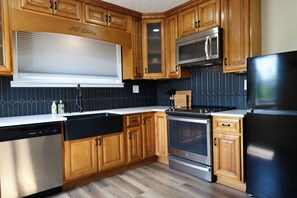 Cozinha moderna com armários de madeira, eletrodomésticos de aço inoxidável e uma geladeira preta.