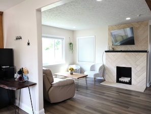 Una sala de estar moderna con chimenea, un televisor montado en la pared y un comedor.