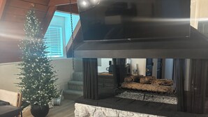 Ein modernes Wohnzimmer mit Kamin aus Stein, einem Weihnachtsbaum und einem flachbildfernseher, der über dem Kamin angebracht ist.