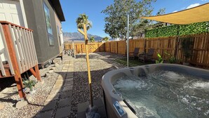 Un patio trasero con un jacuzzi, muebles de jardín, una cerca de madera y vistas a la montaña.