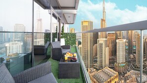 Ein Balkon mit Glastrennwand, Gartenmöbeln und einem Tisch mit Früchten und einem Glas Orangensaft.