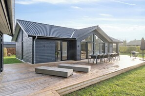 Ett modernt hus med en terrass, utomhusmöbler och en grillplats.