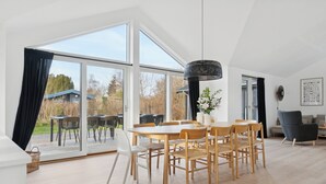 Un vaste espace dédié à la salle à manger, avec une grande table et des chaises, un luminaire suspendu et une vue sur l’extérieur grâce à de grandes portes vitrées.