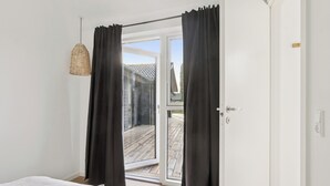 Une chambre avec un lit, une porte-fenêtre coulissante donnant sur une terrasse et un luminaire suspendu.