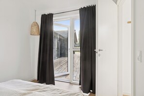 Un dormitorio con cama, puerta corrediza de vidrio a una terraza y una lámpara colgante.