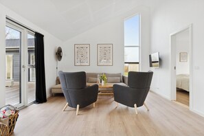Una sala de estar moderna con un sofá, dos sillones, una mesa de centro y un televisor.