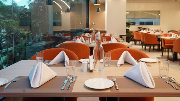 Restaurante com mesas preparadas para refeições, com vista através de amplas janelas.
