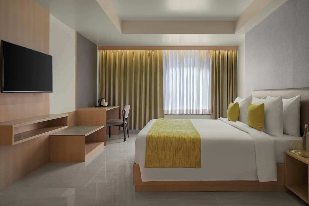 Una habitación de hotel moderna con una cama grande, un televisor de pantalla plana en la pared, un escritorio y una silla.