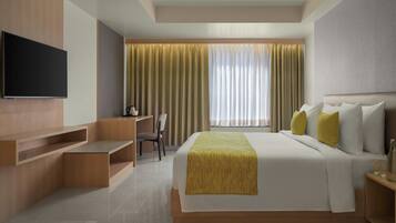 A modern hotel room with a large bed, a flat-screen TV mounted on the wall, a desk, and a chair.