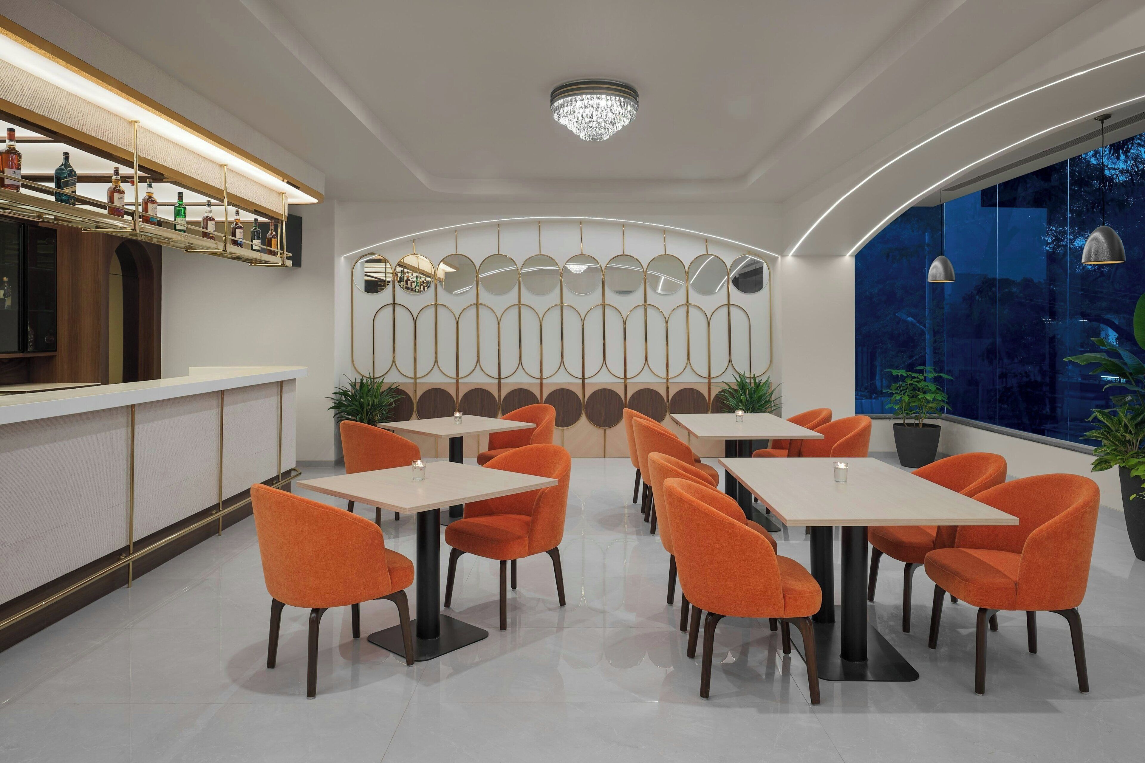 A modern restaurant interior with a bar area, orange chairs, and a decorative wall with mirrors.