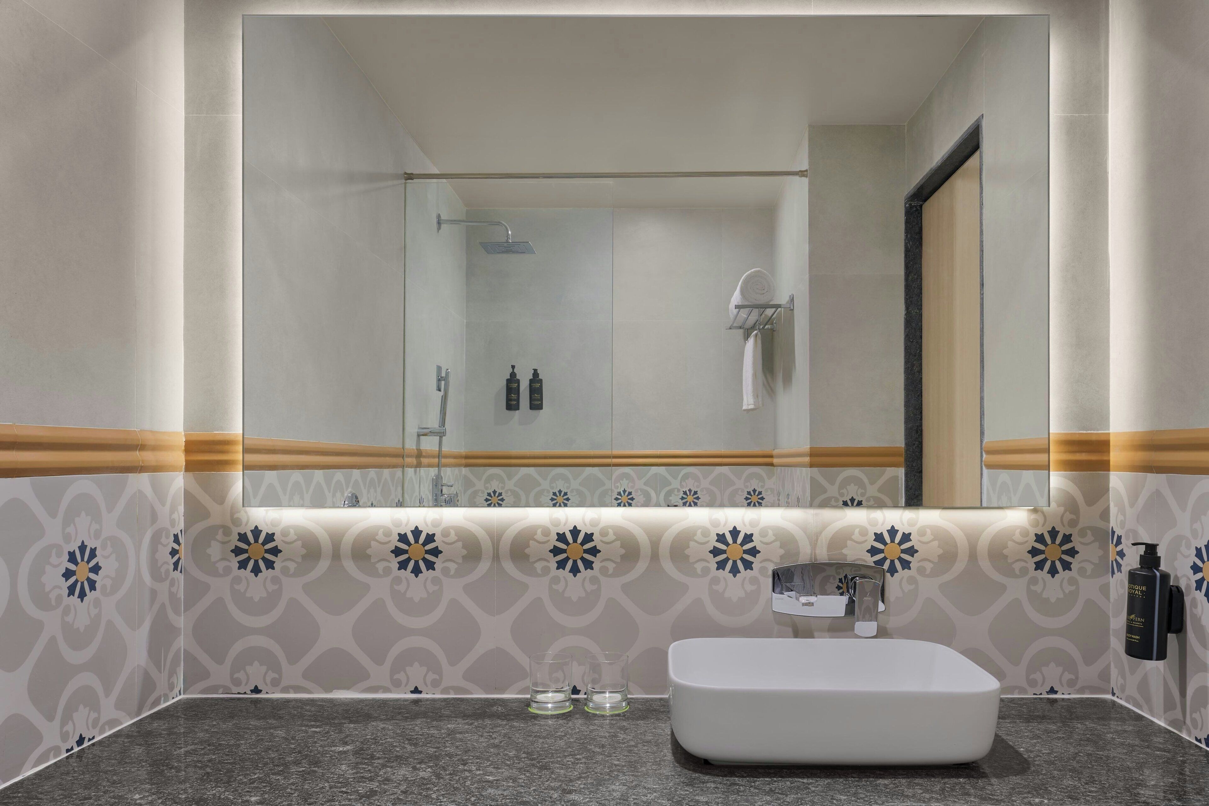 A modern bathroom with a large mirror, a white sink, and a shower area.