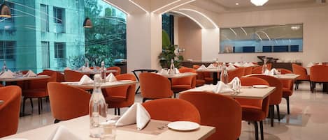 A modern restaurant with orange chairs and tables, large windows, and a clean, well-lit interior.