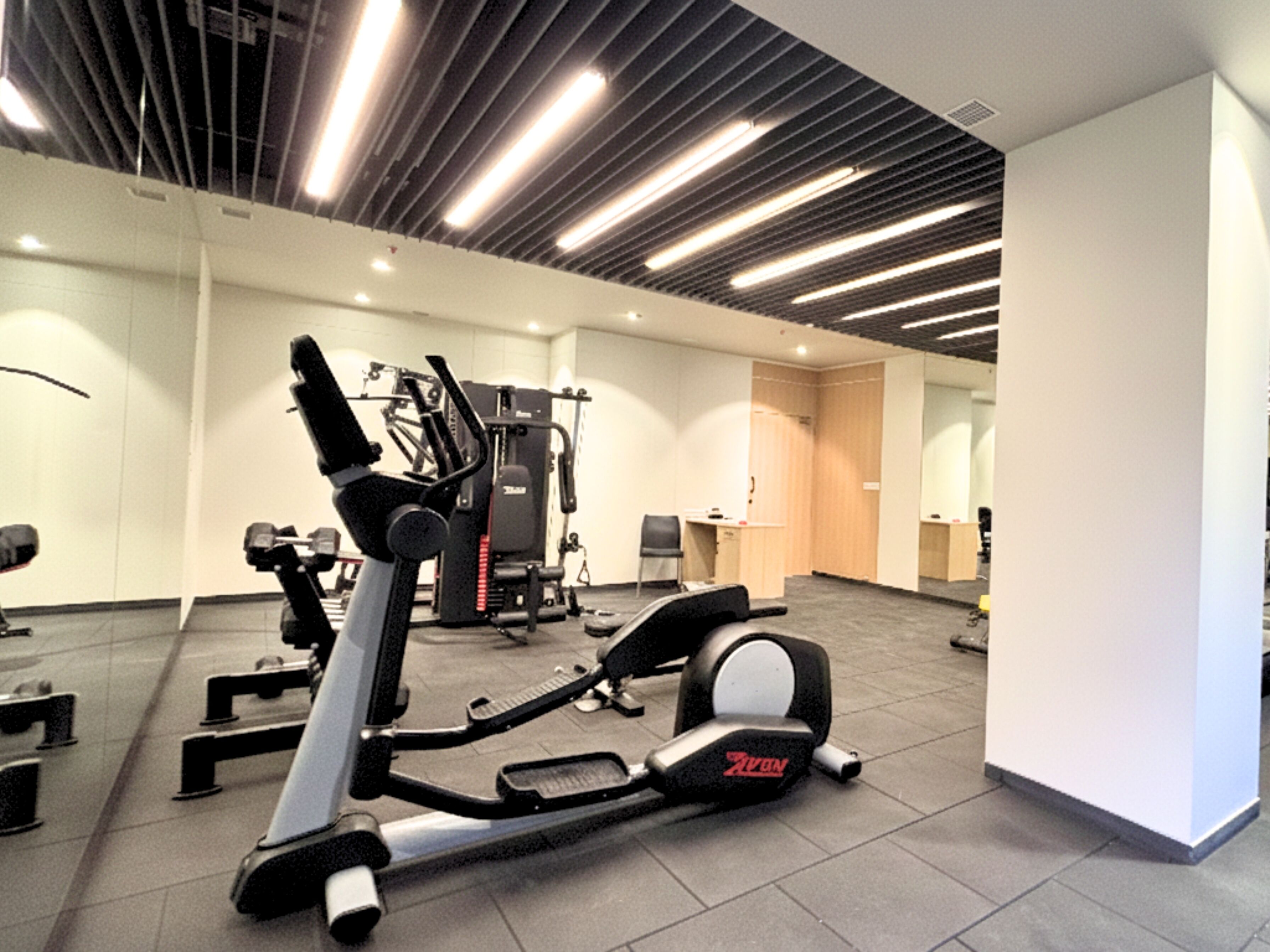 A gym with exercise equipment, including a treadmill and weight machines, and a mirror reflecting the space.