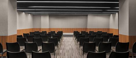 A conference room with rows of black chairs, a carpeted floor, and a wooden accent wall.