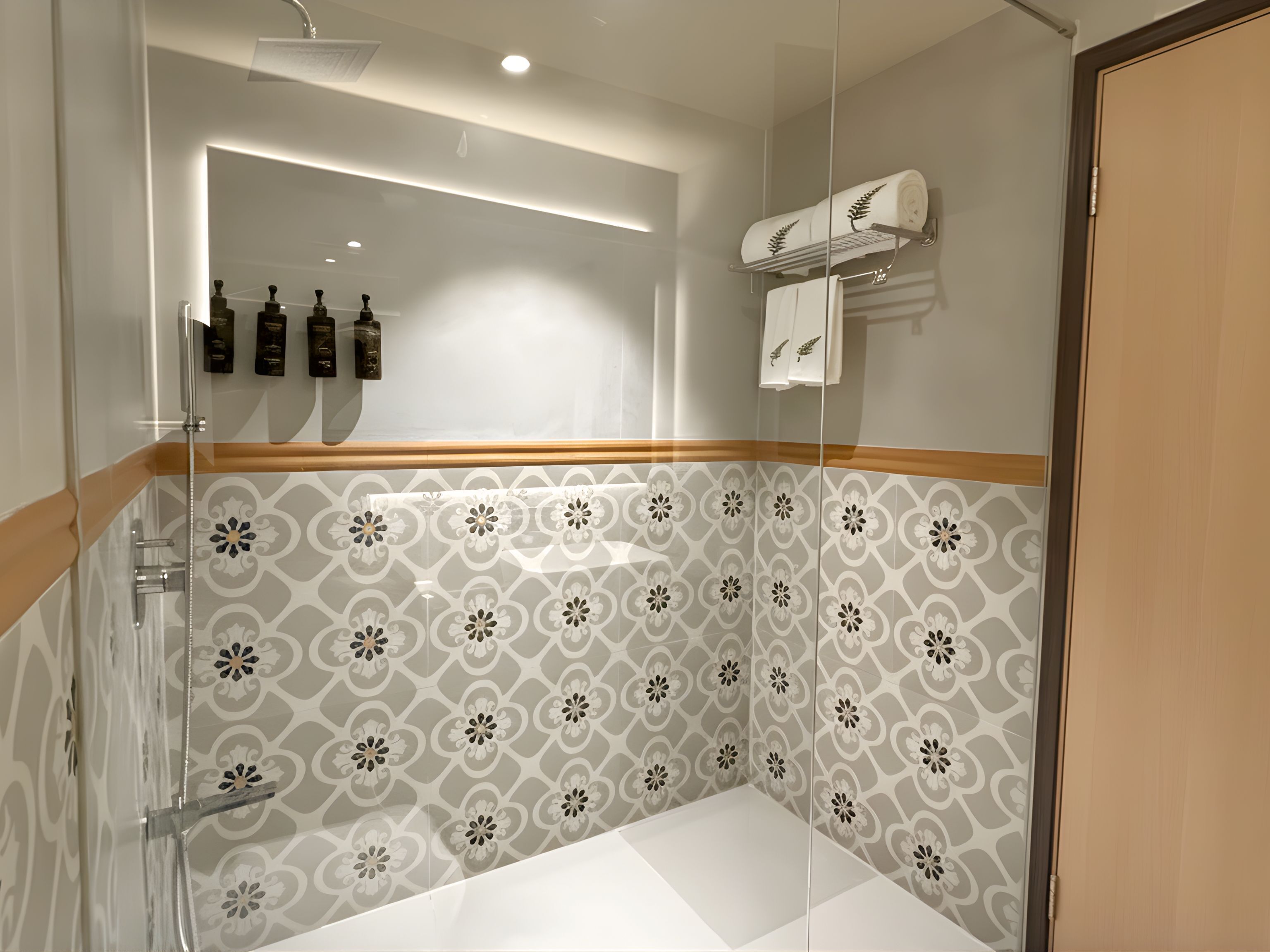 A modern bathroom with a glass shower enclosure, patterned tiles, and a wooden accent strip.