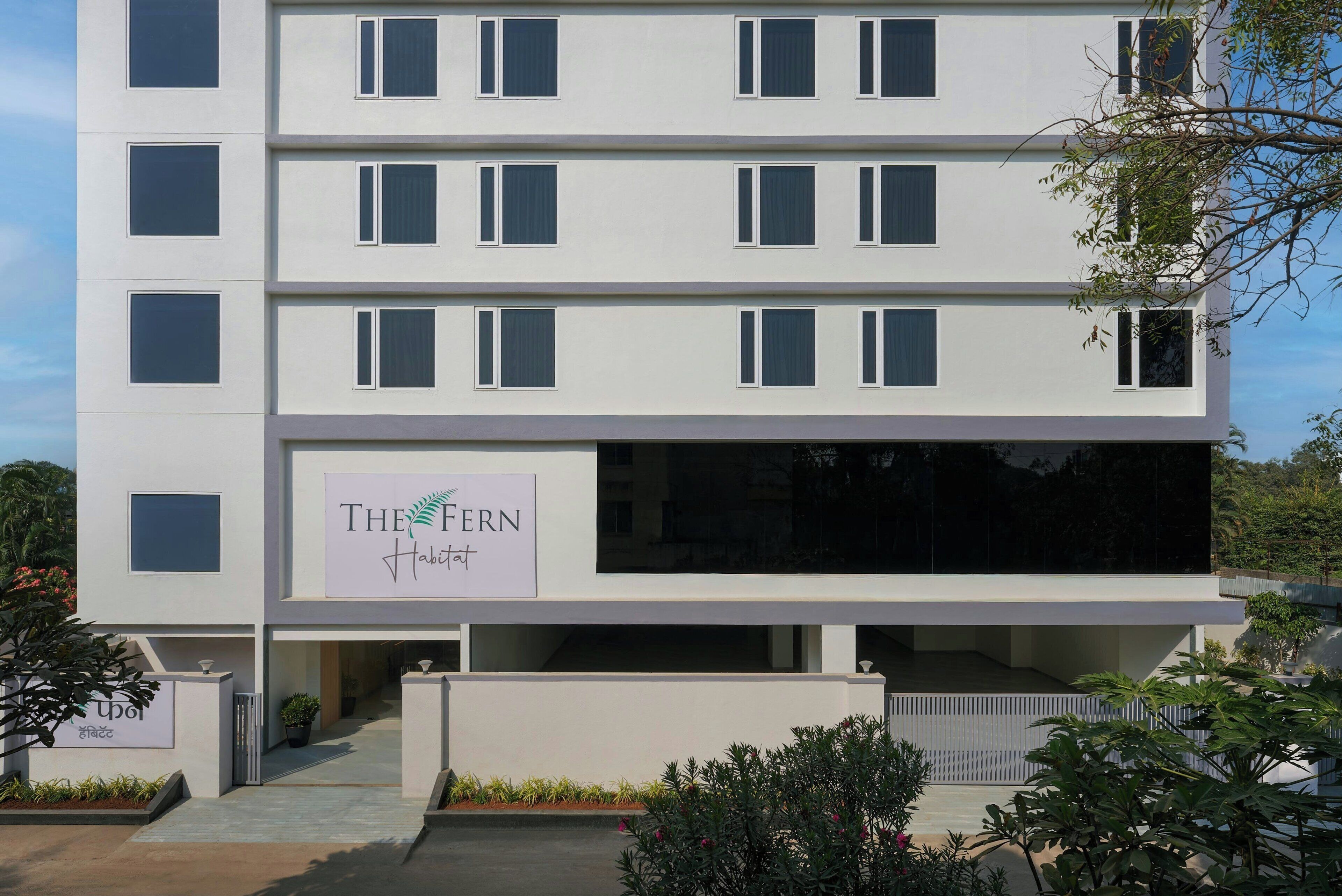 A multi-story hotel with a modern facade, a prominent sign reading "The Fern Habitat," and a gated entrance.