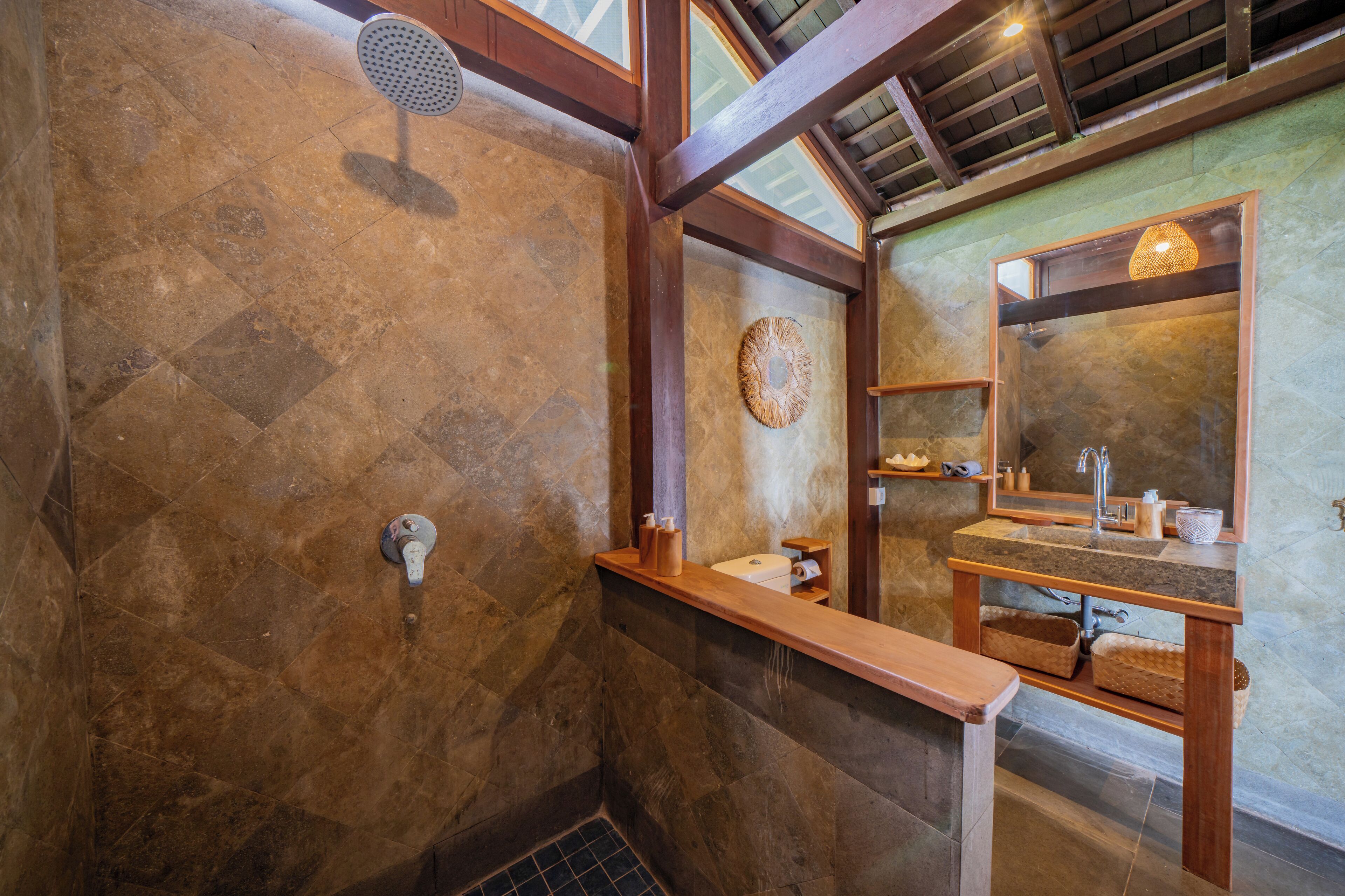 Un bagno con parete in pietra, travi in legno, doccia, lavabo con specchio e portasci.